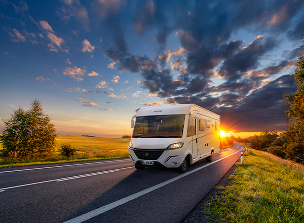 Photo d'un camping-car Intégral Pilote, modèle G740 roulant sur une route avec un coucher de soleil en fond