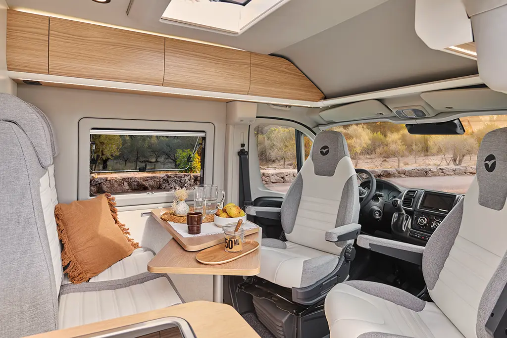 Intérieur d'un fourgon aménagé V630S avec banquette en tissu clair, table en bois et sièges cabine pivotants - décoration Pyla